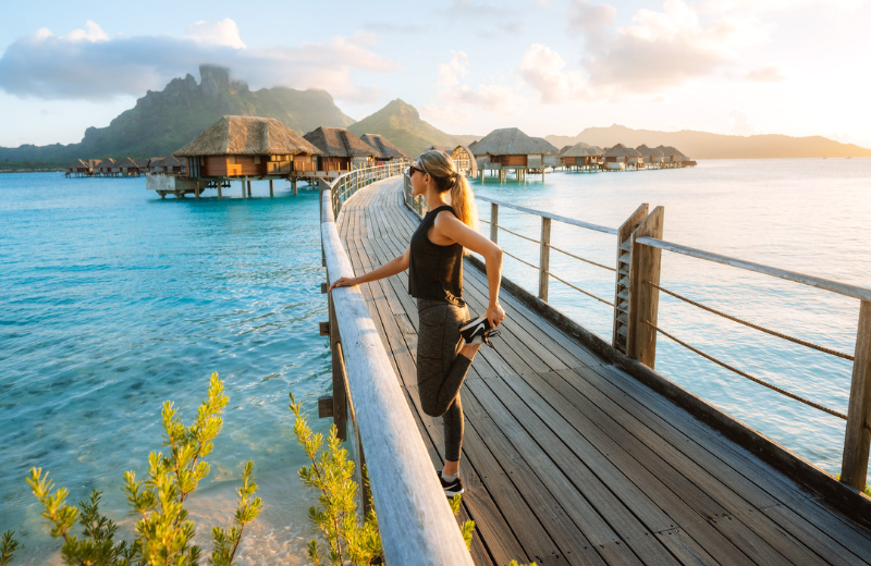 مسافر يرتدي ملابس رياضية حديثة مقاومة للتجاعيد ويجلس بشكل مريح على متن قطار أو طائرة، مع حقيبة ظهر صغيرة مضغوطة بالقرب منه، مع التركيز على الملابس الرياضية الملائمة للسفر وسهولة التعبئة